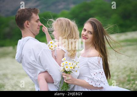 Famiglia felice sul grande prato di montagna camomilla. Scena emozionale, d'amore e di cura. Foto Stock