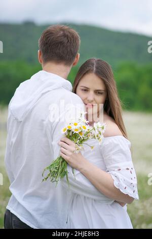 Coppia felice sul grande prato di montagna camomilla. Scena emozionale, d'amore e di cura. Foto Stock