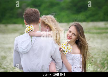 Famiglia felice sul grande prato di montagna camomilla. Scena emozionale, d'amore e di cura. Foto Stock