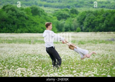 Felice padre giocare con la figlia in grande camomilla prato di montagna. Scena emozionale, d'amore e di cura. Foto Stock