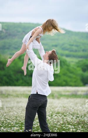 Felice padre giocare con la figlia in grande camomilla prato di montagna. Scena emozionale, d'amore e di cura. Foto Stock