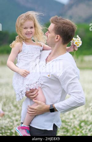 Felice padre e figlia in grande camomilla prato di montagna. Scena emozionale, d'amore e di cura. Foto Stock
