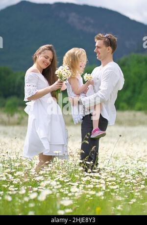 Famiglia felice sul grande prato di montagna camomilla. Scena emozionale, d'amore e di cura. Foto Stock