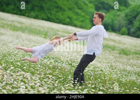 Felice padre giocare con la figlia in grande camomilla prato di montagna. Scena emozionale, d'amore e di cura. Foto Stock