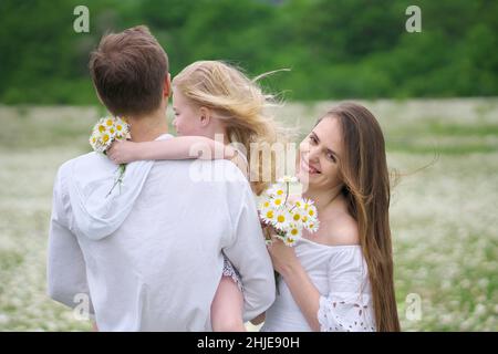 Famiglia felice sul grande prato di montagna camomilla. Scena emozionale, d'amore e di cura. Foto Stock