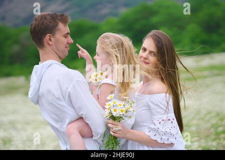 Famiglia felice sul grande prato di montagna camomilla. Scena emozionale, d'amore e di cura. Foto Stock