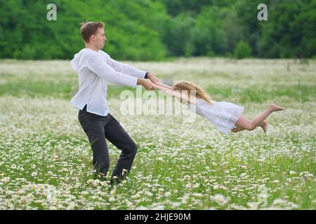 Felice padre giocare con la figlia in grande camomilla prato di montagna. Scena emozionale, d'amore e di cura. Foto Stock