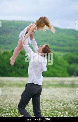 Felice padre giocare con la figlia in grande camomilla prato di montagna. Scena emozionale, d'amore e di cura. Foto Stock