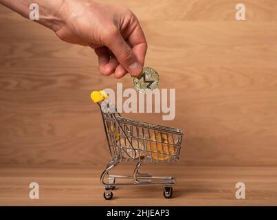 Moneta d'oro Monero in mano maschile, mettendola nel cestino della spesa. pagamenti crypto. Foto Stock