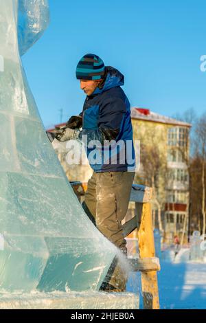 Lo scultore taglia una figura di ghiaccio da un blocco di ghiaccio con uno scalpello PER NATALE su un ponteggio di legno Foto Stock