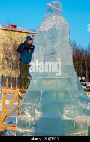Lo scultore taglia una figura di ghiaccio da un blocco di ghiaccio con uno scalpello PER NATALE su un ponteggio di legno Foto Stock