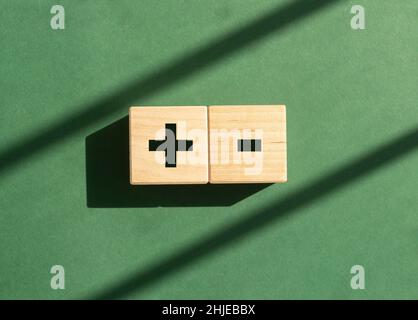Segni più e meno sui dadi su sfondo verde con luce diurna. Concetto di positivo e negativo, pro e contro. Confronto degli opposti. Foto Stock