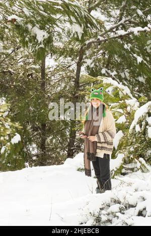 Mevasseret Zion, Israele - 27th gennaio 2022: Una ragazza adolescente in piedi in una foresta nevosa, tenendo il suo smartphone e sorridendo alla macchina fotografica. Foto Stock