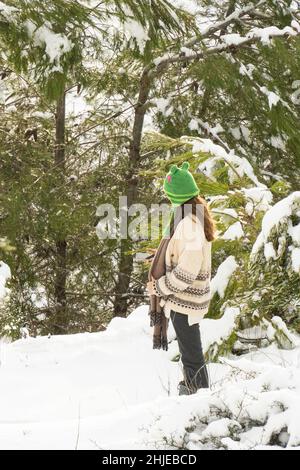 Mevasseret Zion, Israele - 27th gennaio 2022: Una ragazza adolescente in piedi in una foresta di pini nevosi, guardando il suo smartphone. Foto Stock