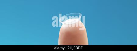 Lente a contatto morbida su dito femmina su sfondo blu Foto Stock