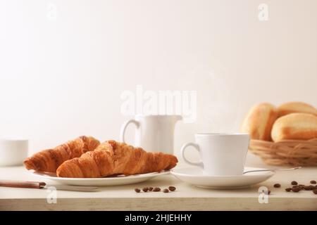 Caffè del mattino su un tavolo di legno bianco con piatto con due croissant e pane con fondo bianco isolato. Vista frontale. Composizione orizzontale. Foto Stock