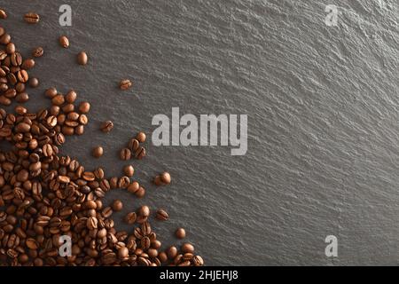 Sfondo scuro con un mucchio di chicchi di caffè naturali selezionati in un angolo su base di ardesia. Vista dall'alto. Composizione orizzontale. Foto Stock