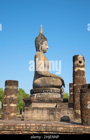 Vista laterale di un'antica scultura di un Buddha seduto sulle rovine di un tempio buddista. Sukhothai City Historical Park, Thailandia Foto Stock