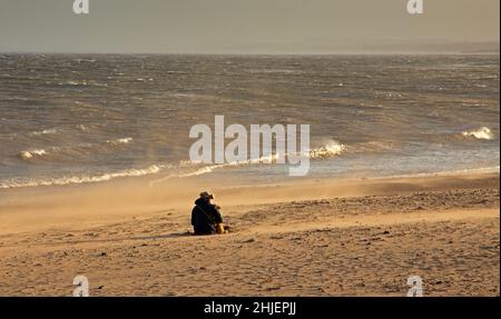 Portobello, Edimburgo, Scozia, Regno Unito. 29th gennaio 2022. Tempesta Malik frustando la sabbia al mare dalla Firth of Forth temperatura di 9 gradi centigradi. Nella foto: La spiaggia di sabbia che si snoda nei forti venti di guastata portati da Storm Malik. Nella foto: Femmina e il suo cane seduto sulla spiaggia circondata da sabbia vorticosa. Credit: Newsandmore/alamy live news. Foto Stock