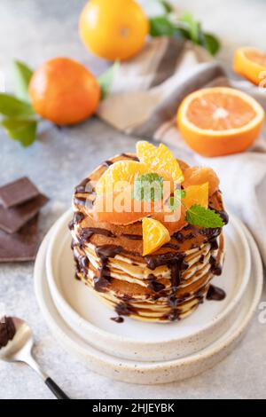 Festeggiamo la giornata di Pancake, colazione sana. Deliziose frittelle di banane americane fatte in casa con cioccolato e arancio rosso su sfondo di pietra grigia. Foto Stock