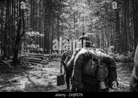 Re-enattori vestiti come soldati tedeschi di fanteria nella seconda guerra mondiale Marching Walking lungo Forest Road nel giorno d'estate. Foto in bianco e nero Foto Stock