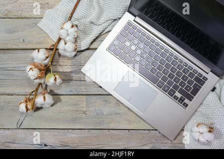 computer portatile con alcune branche di cotone e una sciarpa su un rustico tavolo di legno grigio, lavoro d'affari in autunno, spazio copia, alto angolo di vista dall'alto, Foto Stock