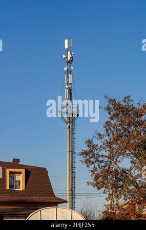 Un'alta torre cellulare con antenne in cima, in una città vicino a edifici residenziali, contro un cielo limpido. Foto Stock