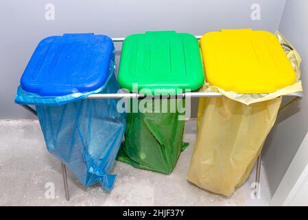 Tre sacchetti per rifiuti per separare vetro, foglio e carta in piedi su una rastrelliera nel garage con il coperchio chiuso. Foto Stock
