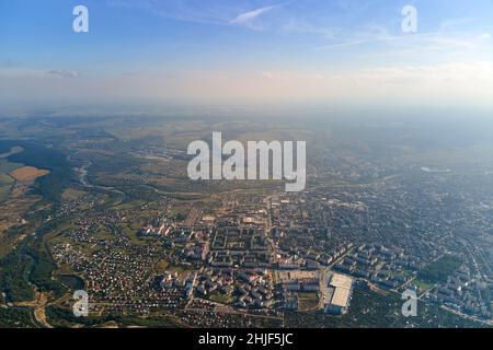 Vista aerea dalla finestra dell'aeroplano ad alta quota della città lontana coperta con strato di smog sottile e nubi distanti in serata. Foto Stock