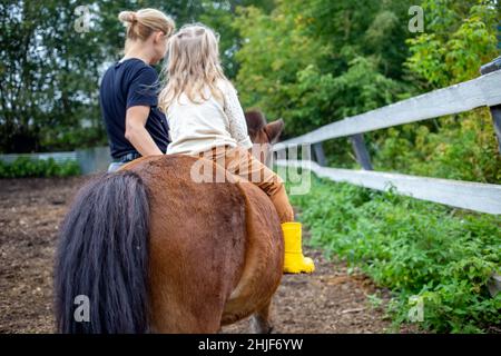 adorabile bambina che cavalca un pony con allenatore. vista posteriore, persone da dietro Foto Stock