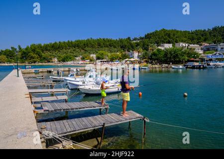 Limenas, Thassos, Grecia - Padre e figlio che pescano nel porto. Barche da pesca e spiaggia balneabile al porto di Limenas. La capitale dell'isola di Thassos Foto Stock
