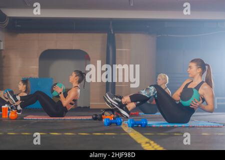 Vista laterale di belle giovani donne che esercitano un tocco russo con palla medica dalla posizione seduta per un abs forte Foto Stock