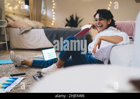 Giovane donna positiva negli occhiali utilizzando un computer portatile durante il lavoro Foto Stock