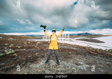 Aurlandsfjellet, Norvegia. Felice giovane donna Tourist Traveler fotografo con fotocamera Camminare vicino a Aurlandsfjellet Scenic Percorso Road. Uno stile di vita attivo Foto Stock