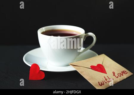 Tazza di tè bianca su sfondo nero. Bustine di tè a forma di cuore. Messa a fuoco selettiva. Foto Stock