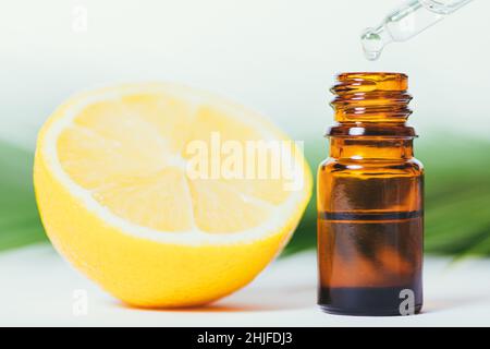 Olio essenziale di limone che gocciola in bottiglia con contagocce accanto a mezzo limone su sfondo bianco, primo piano Foto Stock