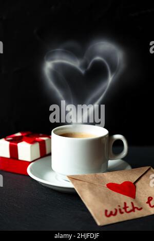 Tazza bianca di caffè espresso con fumo a forma di cuore. Sfondo nero, messa a fuoco selettiva, tonalità. Foto Stock