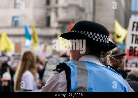 Londra,UK-28 ago 2021: Poliziotto biondo femminile a Londra che osserva una grande protesta in background. Foto Stock