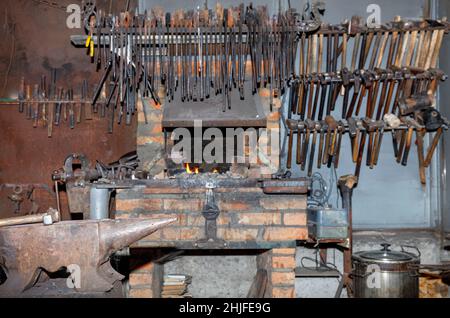 Il martello del fabbro si trova su un'incudine metallica all'interno di un'antica bottega del fabbro in sfocatura. Foto Stock