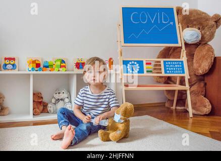 Carino bambino ragazzo in quarantena casa giocando medico sul pavimento con i suoi orsacchiotti malati indossare maschere mediche durante coronavirus COVID-2019 focolaio Foto Stock