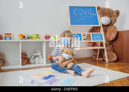 Carino bambino ragazzo in quarantena casa giocando medico sul pavimento con i suoi orsacchiotti malati indossare maschere mediche durante coronavirus COVID-2019 focolaio Foto Stock