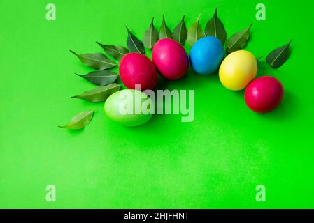 Disegno di Pasqua su sfondo verde. Uova multicolore e foglie verdi giovani. Spazio di copia per il testo. Foto Stock