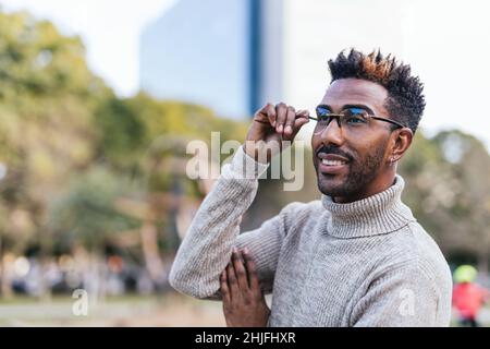 Ritratto di sognante afroamericano in gilet dolcevita che cattura i suoi bicchieri con la mano Foto Stock