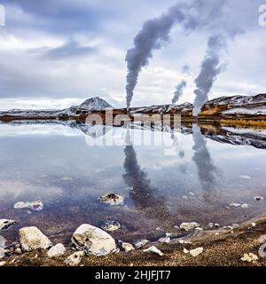 Produzione di energia nella zona geotermica di Bjarnarflag dell'Islanda settentrionale. Riflessione speculare nel lago blu, con il monte Namfjoll e prugna a vapore Foto Stock