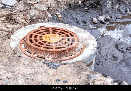 Borovichi, Russia - 10 agosto 2021: Copertura in metallo arrugginito per tombini su strada urbana. Pozzetto di drenaggio circolare per fognature Foto Stock