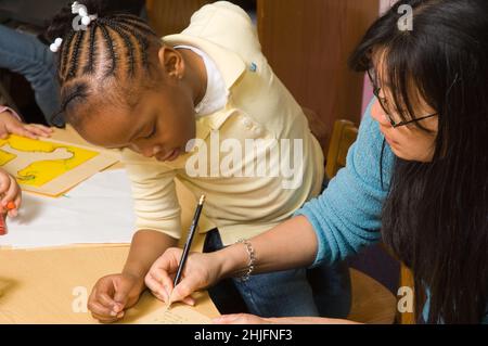 Istruzione Preschool classe 4-5 anni insegnante femminile con ragazza che scrive ciò che la ragazza vuole dire sul suo disegno Foto Stock