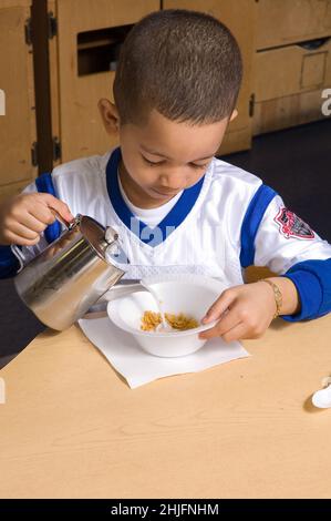 Istruzione Preschool classe età 4-5 pasto tempo colazione ragazzo versare il latte nella sua ciotola di cereali Foto Stock