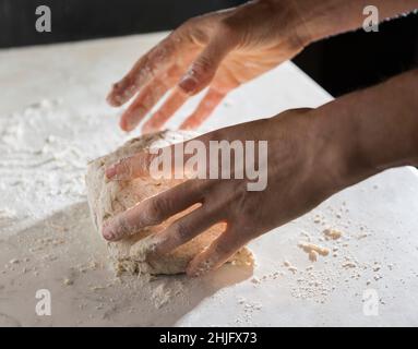 Preparazione del pane fatta in casa in Toscana con farina biologica su tavola bianca. Le mani delle donne preparano l'impasto del pane. Foto Stock