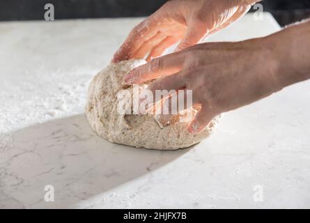 Preparazione del pane fatta in casa in Toscana con farina biologica su tavola bianca. Le mani delle donne preparano l'impasto del pane. Foto Stock