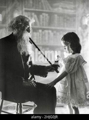 Fitz W. Guerin Fotografia intitolata Girl Lghting Long Pipe of Old Bearded Man - ambientato in biblioteca o studio come sfondo di scaffale del libro - circa 1902 Foto Stock